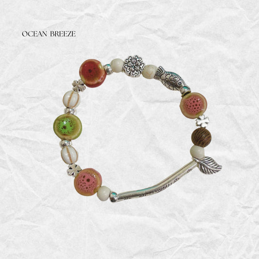 Handcrafted beaded bracelet featuring colorful ceramic beads, silver fish charm, and natural accents, inspired by ocean breezes and bohemian style.